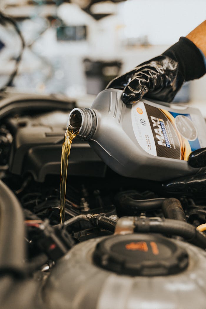 Home Close-up of a mechanic's gloved hand pouring engine oil into a vehicle.