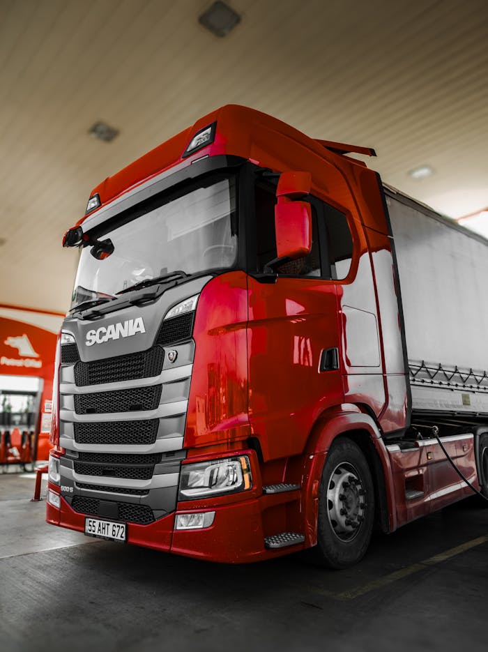Menu Bright red Scania truck parked at a fuel station with modern design and clean lines.