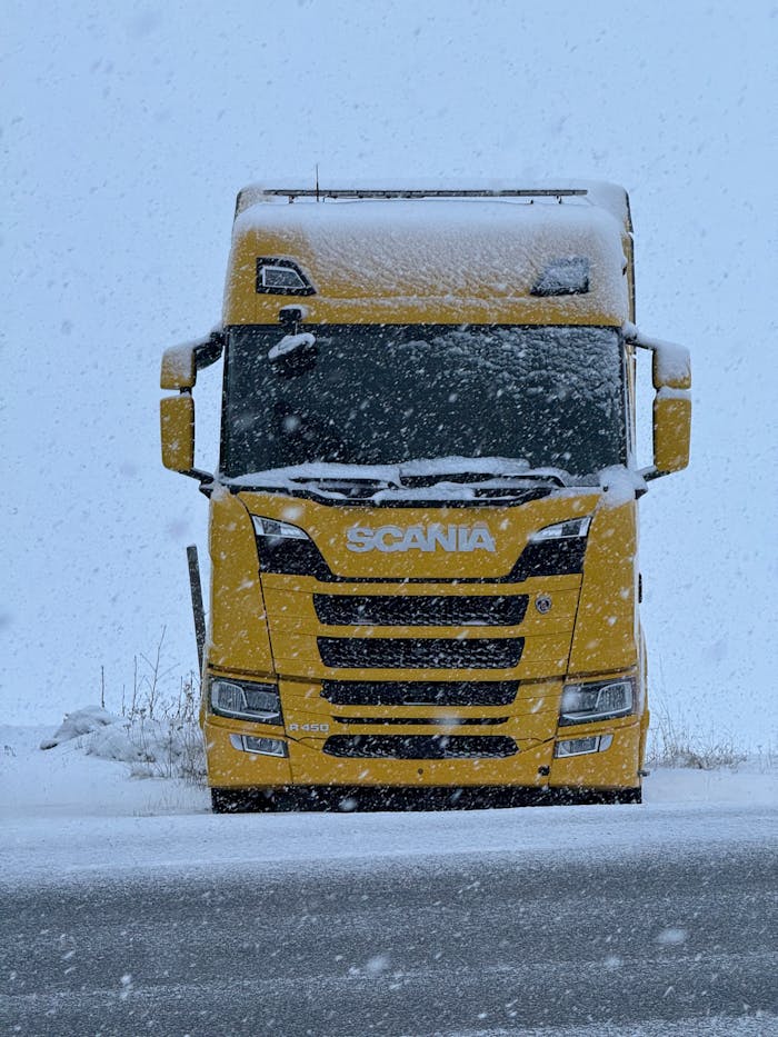 Home A yellow Scania truck parked on a snowy road during a winter snowfall.