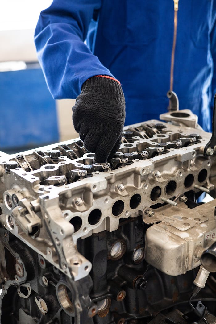 Home Close-up of a mechanic in gloves working on a car engine cylinder head in a workshop setting.